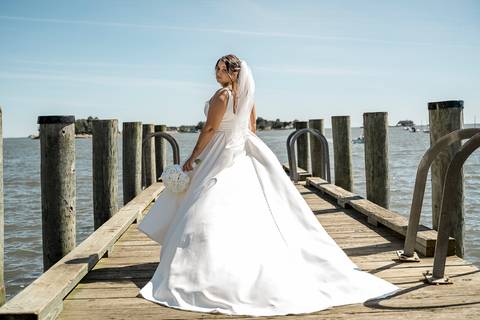 The bride gracefully walking along the shoreline at Stony Creek, her flowing gown swaying in the gentle breeze, with the serene ocean stretching out behind her.'