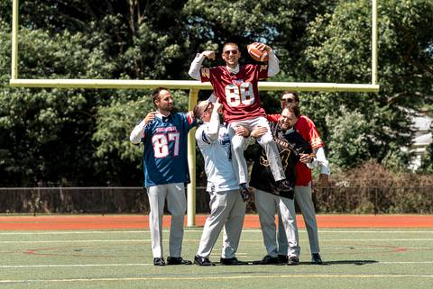 Groom and groomsmen laughing and posing on a football field, with Vinny holding a football—honoring his role as a coach before the wedding ceremony.'
