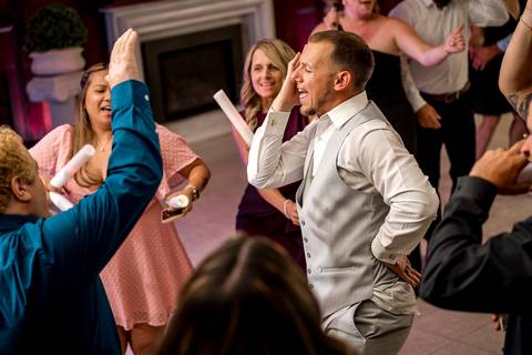 Bridesmaids and groomsmen letting loose on the dance floor, captured mid-laugh in a lively celebration moment.'