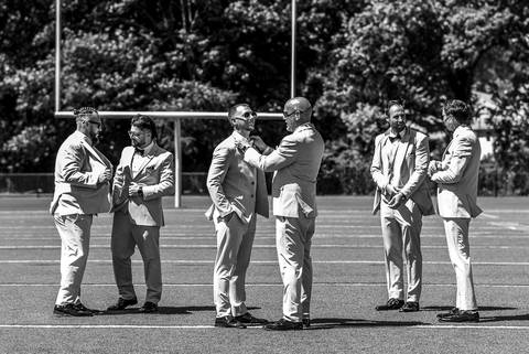 Groom and groomsmen laughing and posing on a football field, with Vinny holding a football—honoring his role as a coach before the wedding ceremony.'