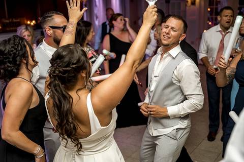 Bride twirling on the dance floor with her dress flowing, surrounded by cheering friends and family.'