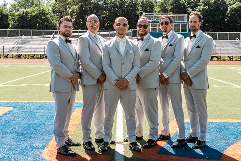 Groom and groomsmen laughing and posing on a football field, with Vinny holding a football—honoring his role as a coach before the wedding ceremony.'