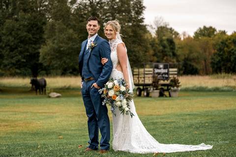 The newlyweds share a romantic first dance under twinkling lights at StoneHurst’s rustic barn, surrounded by cheering guests, while warm autumn colors fill the space with a cozy, festive atmosphere.'