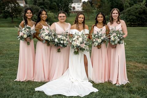 The bridesmaids wear matching pink dresses, each holding a delicate bouquet as they smile together in a joyful wedding moment.'