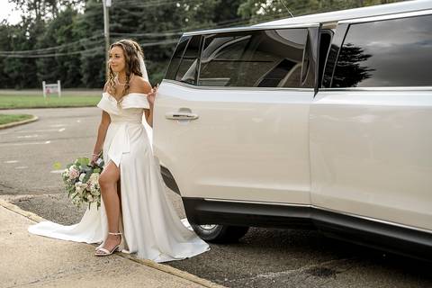 The bride rides in a classic white limousine on her way to the church, holding her bouquet as she prepares for the ceremony.'