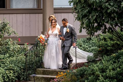 The bride walks down the aisle between her proud parents, sunlight pouring over the Heritage Hotel garden in Southbury, CT — pure elegance and emotion.'