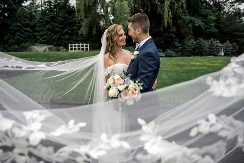 The newlyweds share a laugh as their veil catches the breeze, symbolizing the lightness of their love.'