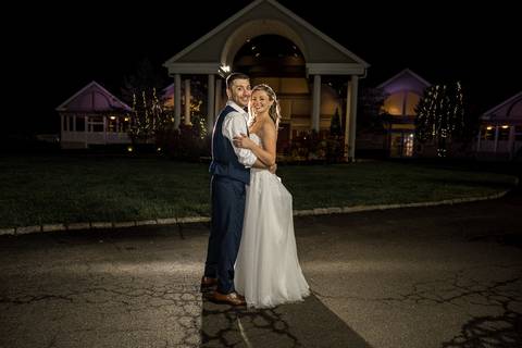 A romantic night shot of the couple under twinkling lights outside The Woodwinds.'