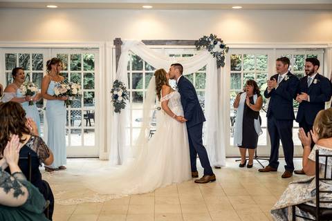 A joyful first kiss as husband and wife, with family and friends cheering in the background.'