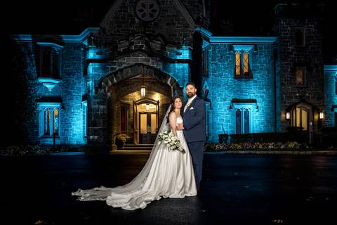 Cinematic night shot of the couple with the illuminated castle in the background, rain creating a magical atmosphere, by Vanessa Trettel Photography.'