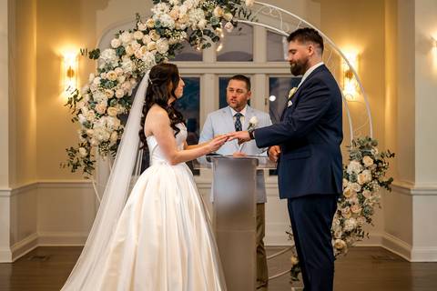 The couple placing rings on each other’s fingers, symbolizing their union during the indoor ceremony at Whitby Castle, photo by Vanessa Trettel Photography.'