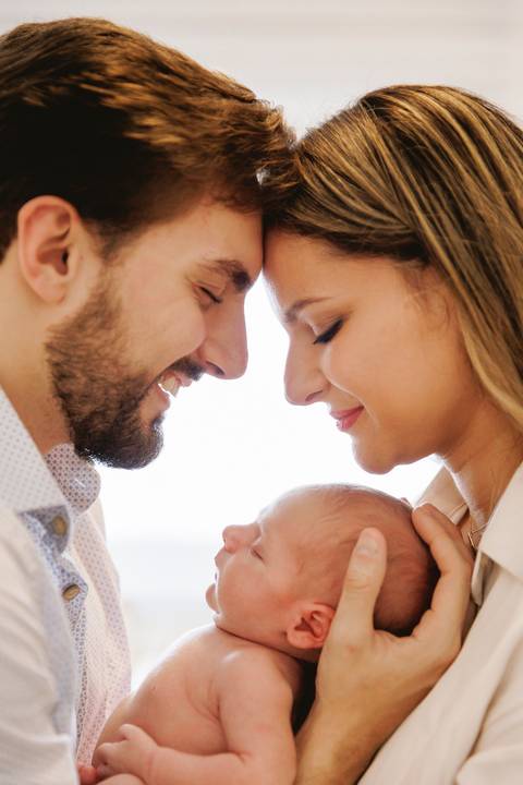 bebê no colo dos pais no contraluz da janela'