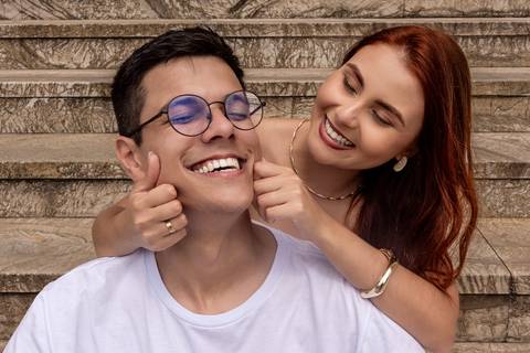 Júlia brinca com o rosto de Leonardo enquanto os dois riem durante ensaio pré wedding espontâneo.'