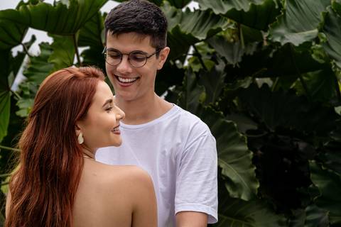 Júlia e Leonardo sorriem juntos entre folhagens durante ensaio de casal nos jardins do MAM no Rio de Janeiro.'