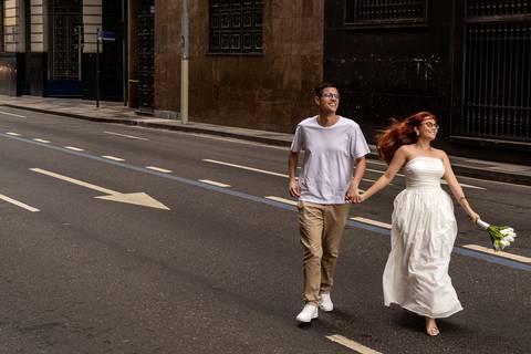 Casal caminha sorrindo pelo Centro do Rio de Janeiro durante ensaio pré wedding urbano.'