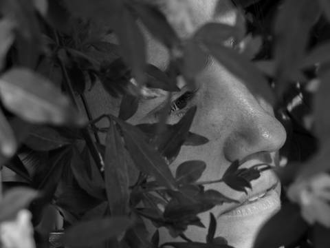 chica-mira-a-traves-de-algunas-hojas-mirada-lejana-fotografía-blanco-y-negro-fotógrafa-irene-lblanc'