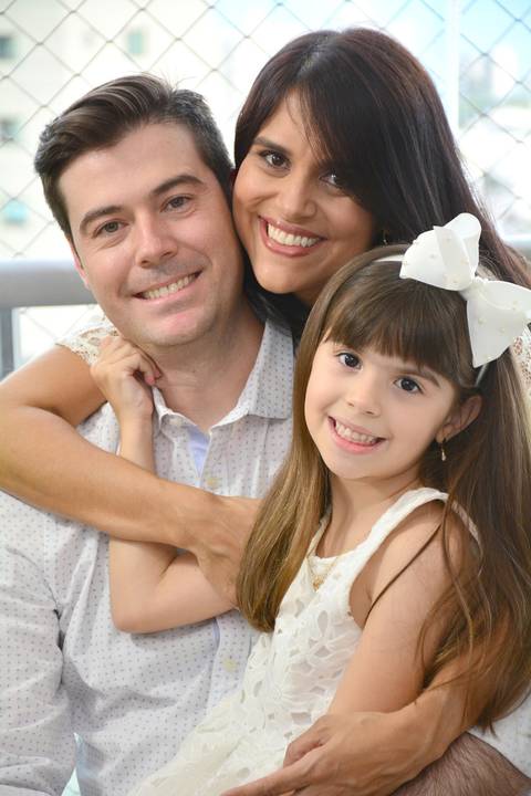 Imagem colorida, onde o casal e sua filha estão abraçados'