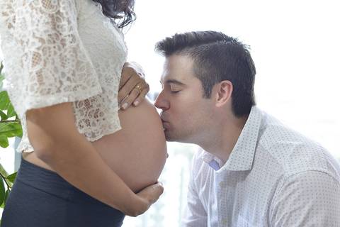 Imagem colorida, onde o pai, de olhos fechados, beija a barriga da mamãe'