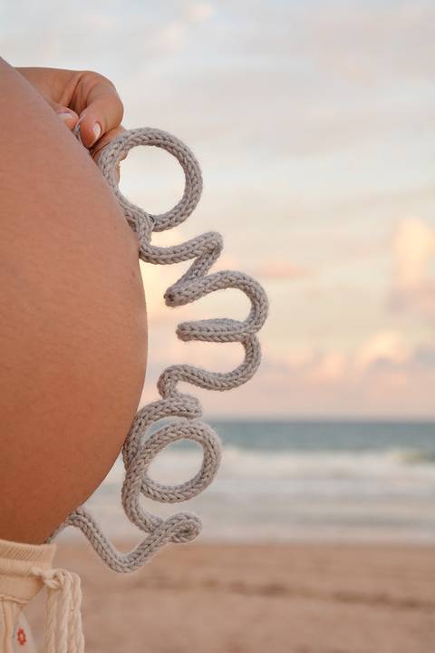 Barriga da mamãe circundada pela palavra AMOR em um aramado com crochê'