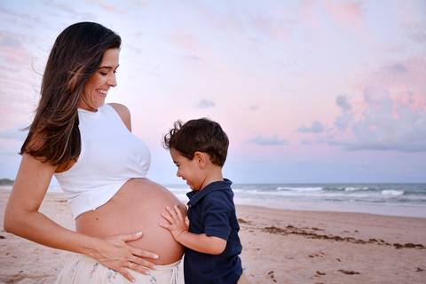 O irmãozinho abraçando a barriga da mamãe na praia'