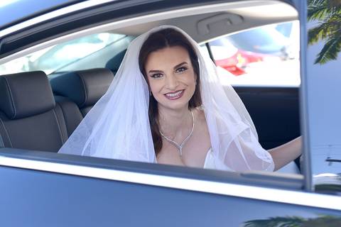 Foto em cor, noiva dentro do carro, vista pela janela.'