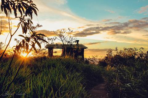 foto em cores de um belíssimo pôr do sol por detrás deum casebre na Chapada'