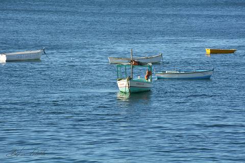 foto em cores praia mansa com pequenos barcos parados no mar'