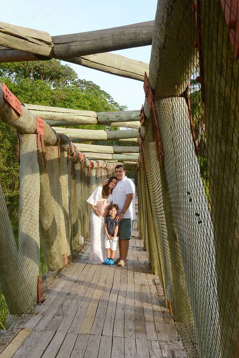 Fotografia do casal gestante com o filho primogênito numa ponte de madeira'