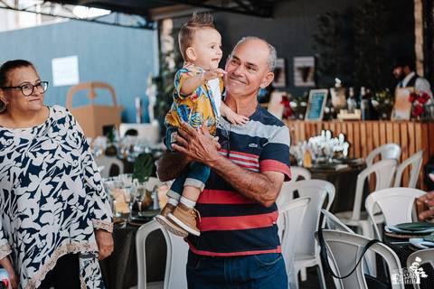 foto espontânea em festa de aniversário infantil de 1 ano, com avô segurando o bebê e sorrindo'