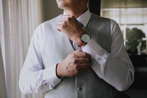 Foto do noivo durante o making of, ajustando o punho da camisa enquanto se arruma para o casamento'