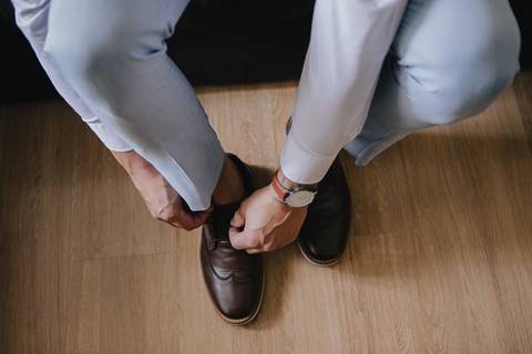 Foto do noivo durante o making of, ajustando o sapato enquanto se arruma para o casamento'