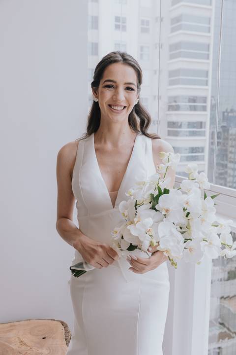 Foto da noiva pronta com o buque de flores nas mãos olhando para a câmera e sorrindo'