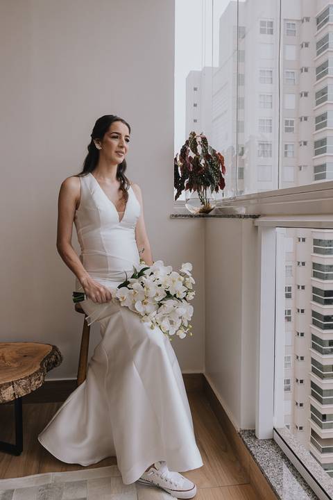 Foto da noiva sentada admirando a paisagem em uma vista alta, de dentro de um apartamento'