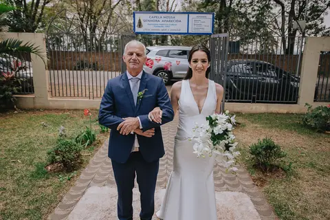 Foto da noiva chegando na cerimônia de casamento de braço dado com o pai'
