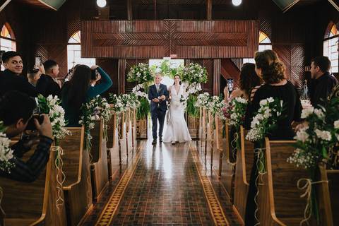 Foto da noiva entrando na capela Nossa Senhora Aparecida, de braço dado com o pai, na primeira parte do cortejo da noiva'