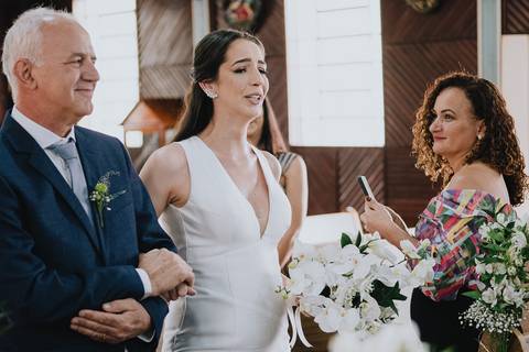 Foto da noiva entrando na capela Nossa Senhora Aparecida, de braço dado com o pai, chorando emocionada durante o cortejo'