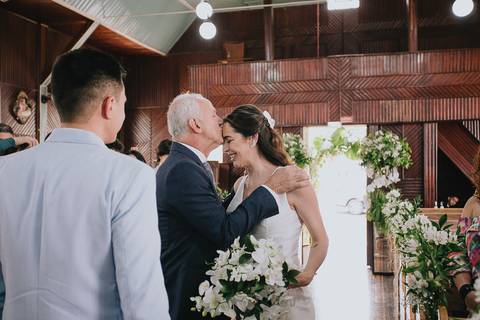 Foto da noiva entrando na capela Nossa Senhora Aparecida, com o pai dando um beijo na testa da noiva'