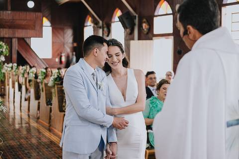 Foto do casal durante a cerimônia de matrimônio na Capela Nossa Senhora Aparecida, com os noivos abraçados e sorrindo'
