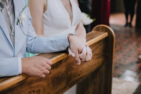 Foto do casal durante a cerimônia de matrimônio na Capela Nossa Senhora Aparecida, no momento da benção da família sobre o casal'
