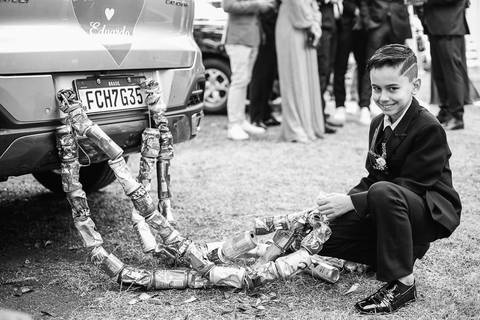 Foto do carro dos noivos com latinhas presas ao carro, em preto e branco, com menino arrumando as latinhas'