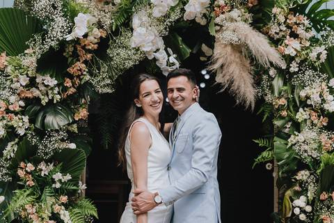 Retrato formal do casal recém casado na frente do arco de flores decorado na capela nossa senhora aparecida'