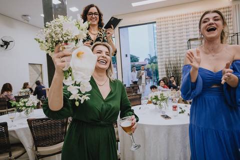 Foto do casamento civil no Espaço Atlanta, da noiva jogando o buquê de flores para as mulheres solteiras e um convidada com o buquê nas mãos'