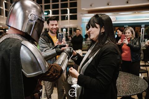 noiva surpreendida em pedido de casamento geek inspirado em star wars, the mandalorian, noivo ajoelhado segurando as alianças, vestido de mandaloriano'