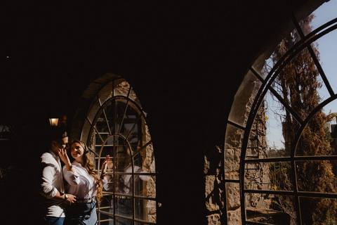 Casal em ensaio pré-wedding na Vinícola La Dorni em Bandeirantes, PR, iluminados pela luz natural ao lado de janelas arqueadas em pedra, em composição artística e intimista'
