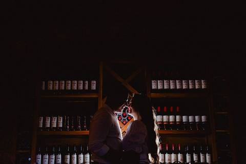 Casal em ensaio pré-wedding na Vinícola La Dorni em Bandeirantes, PR, em silhueta entre prateleiras de vinhos, em cena romântica e intimista'