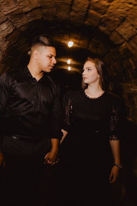 Casal em ensaio pré-wedding na Vinícola La Dorni, Bandeirantes (PR), caminhando de mãos dadas pelo túnel de pedras com motion blur artístico e flash marcado, criando expressão intensa e clima cinematográfico'