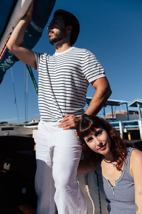 Retrato editorial do casal no veleiro: Arthur em pé de mão na cintura, Mari apoiada nele, pré-wedding estilo náutico'