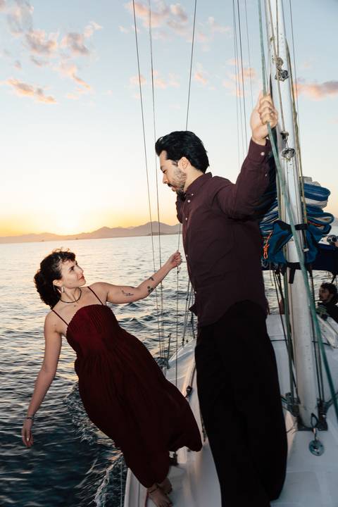 Arthur segura Mari em pose de dança sobre o convés do veleiro, vestido vinho, luz do pôr do sol em Pontal do Paraná'