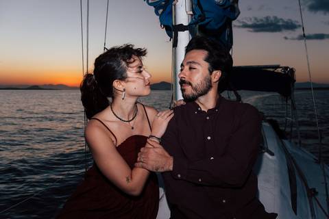 Casal em vestido vinho se abraça ao entardecer, cores do pôr do sol ao fundo, ensaio pré-wedding em veleiro'