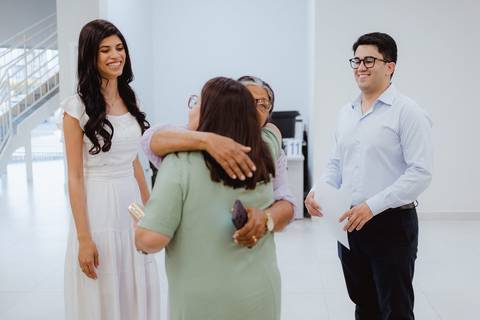 Noiva rindo espontaneamente enquanto parentes se abraçam ao fundo'